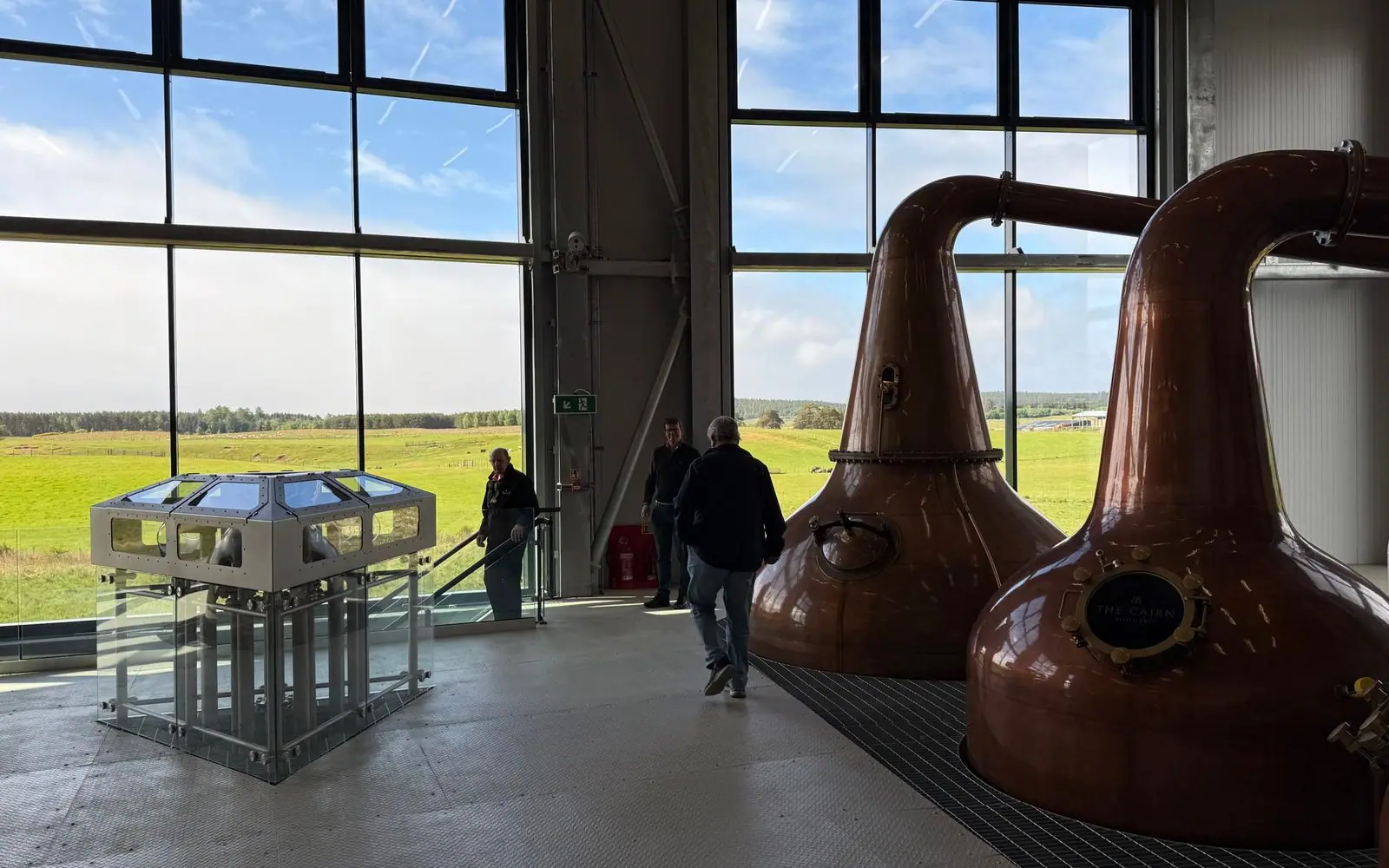 Gleaming copper pot still inside a rustic distillery with warm light raking across the hammered metal and timber beams
