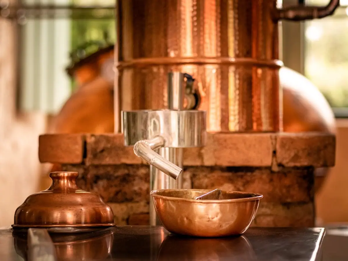 Close detail of a hand-riveted copper still neck and condenser coil glowing under workshop lights